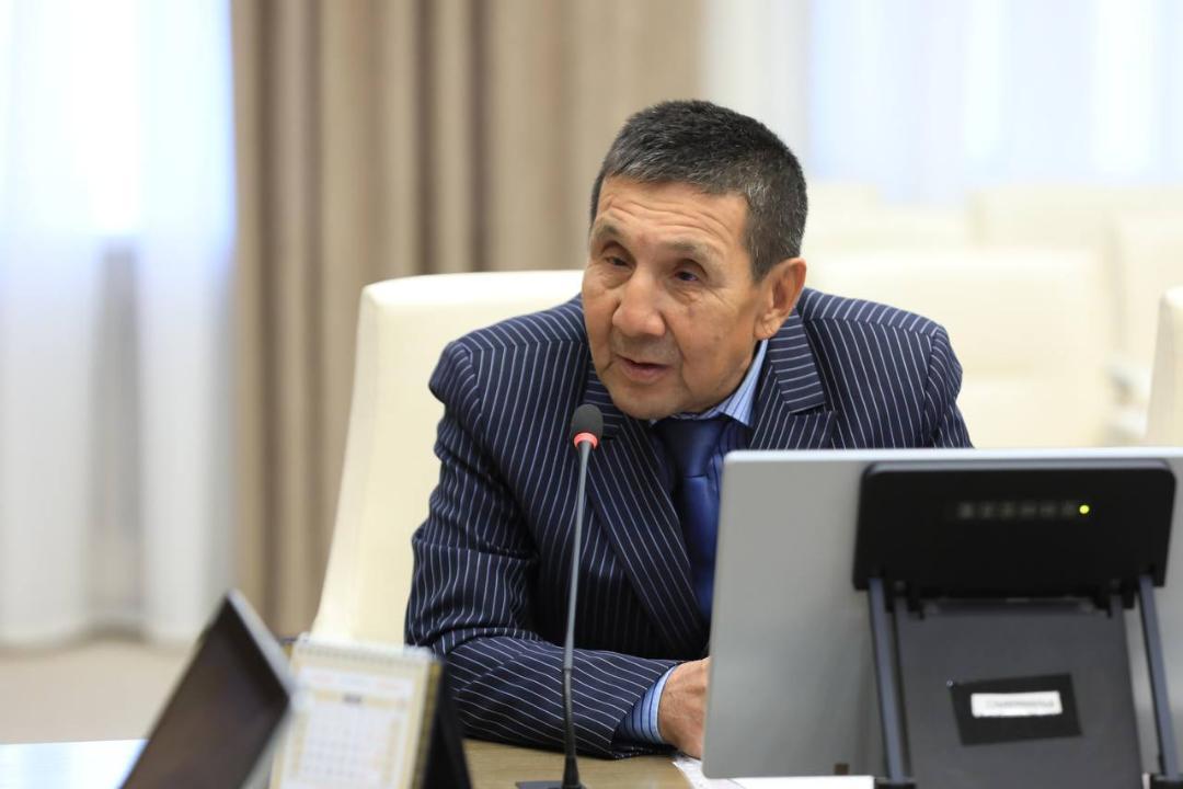 Көк жолақты костюм киген ер адам микрофонның алдында сөйлеп тұр.