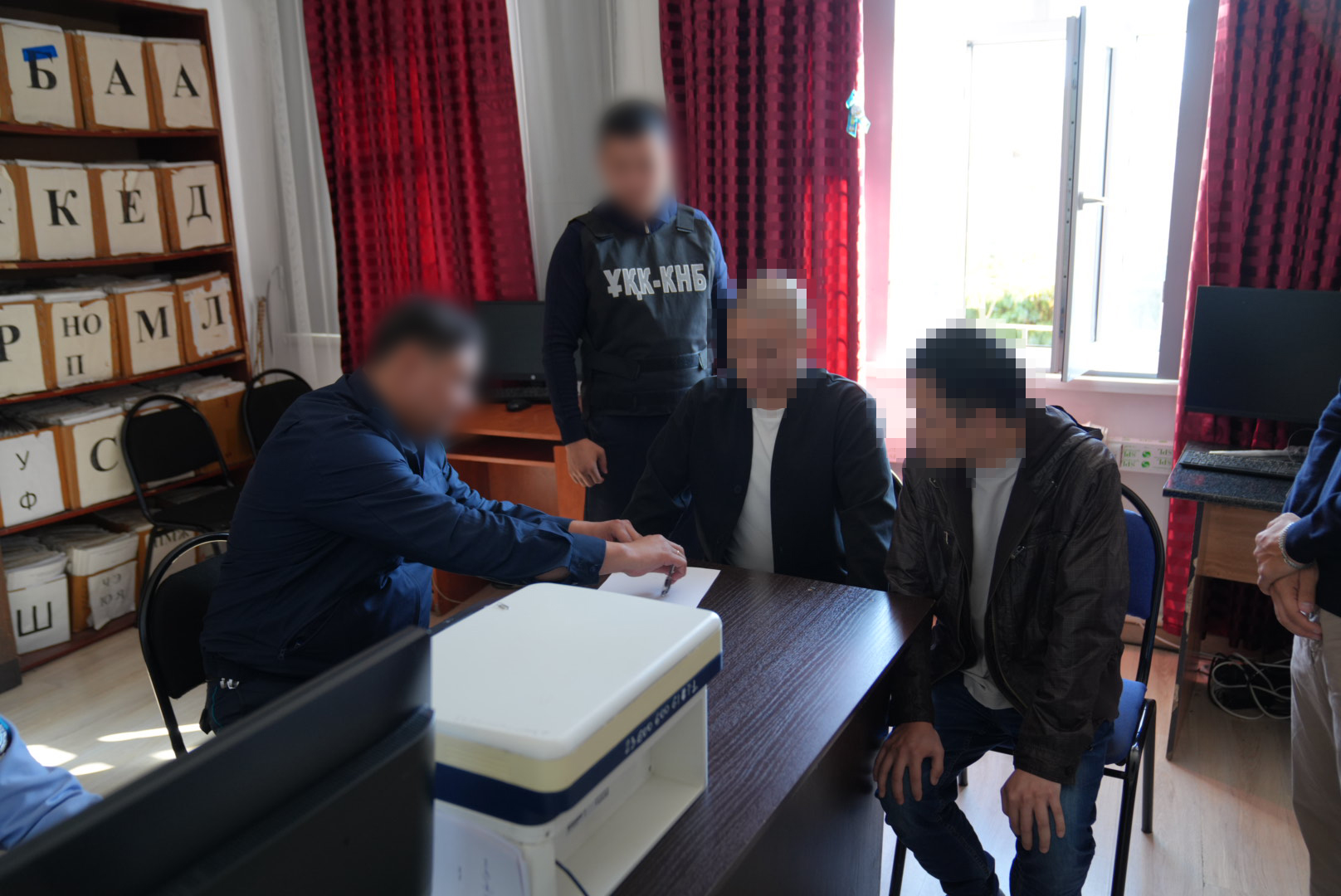 Сотрудники правоохранительных органов проводят допрос двух мужчин в кабинете. Лица людей размыты.