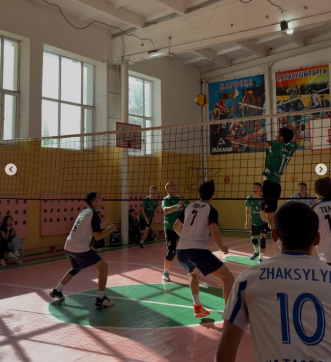 Спорт залында волейбол ойынының барысы: ойыншылардың топ үшін күресі.