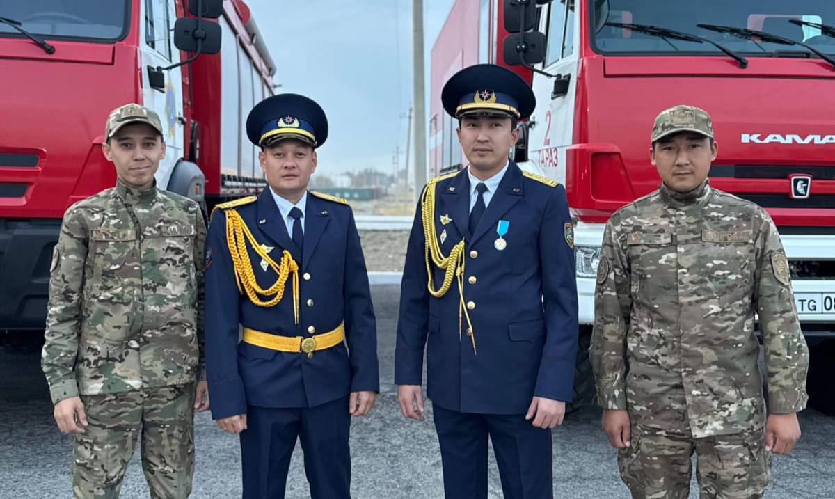 Екі әскери формадағы және екі параделік киімдегі ер адамдардың қызыл өрт сөндіру көліктерінің алдында тұрған суреті.