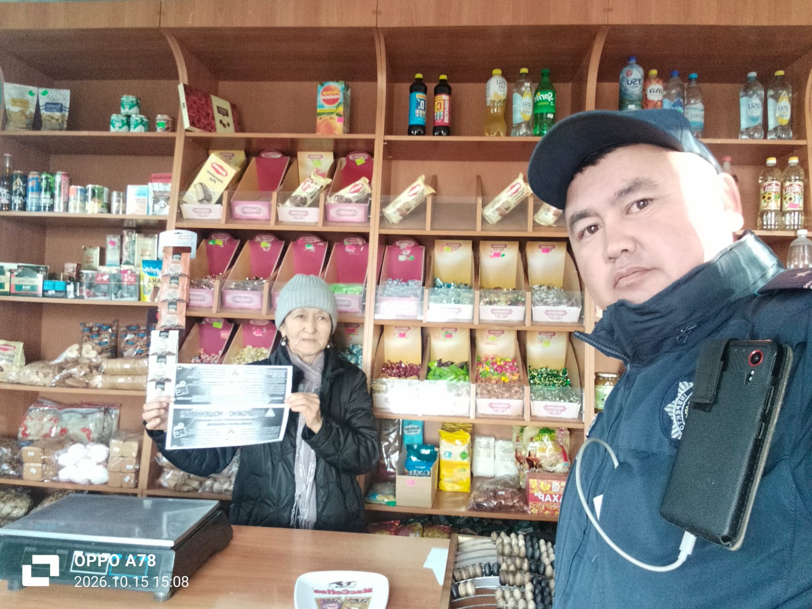 Дүкенде ақпараттық парақ ұстаған әйел және жанында тұрған полиция қызметкері.
