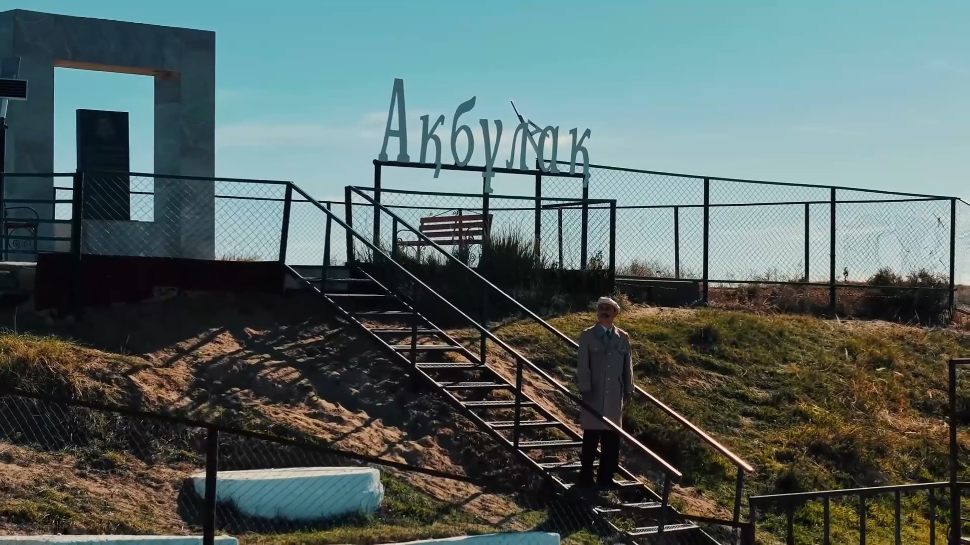 «Ақбұлақ» жазуы бар баспалдақта тұрған адам.