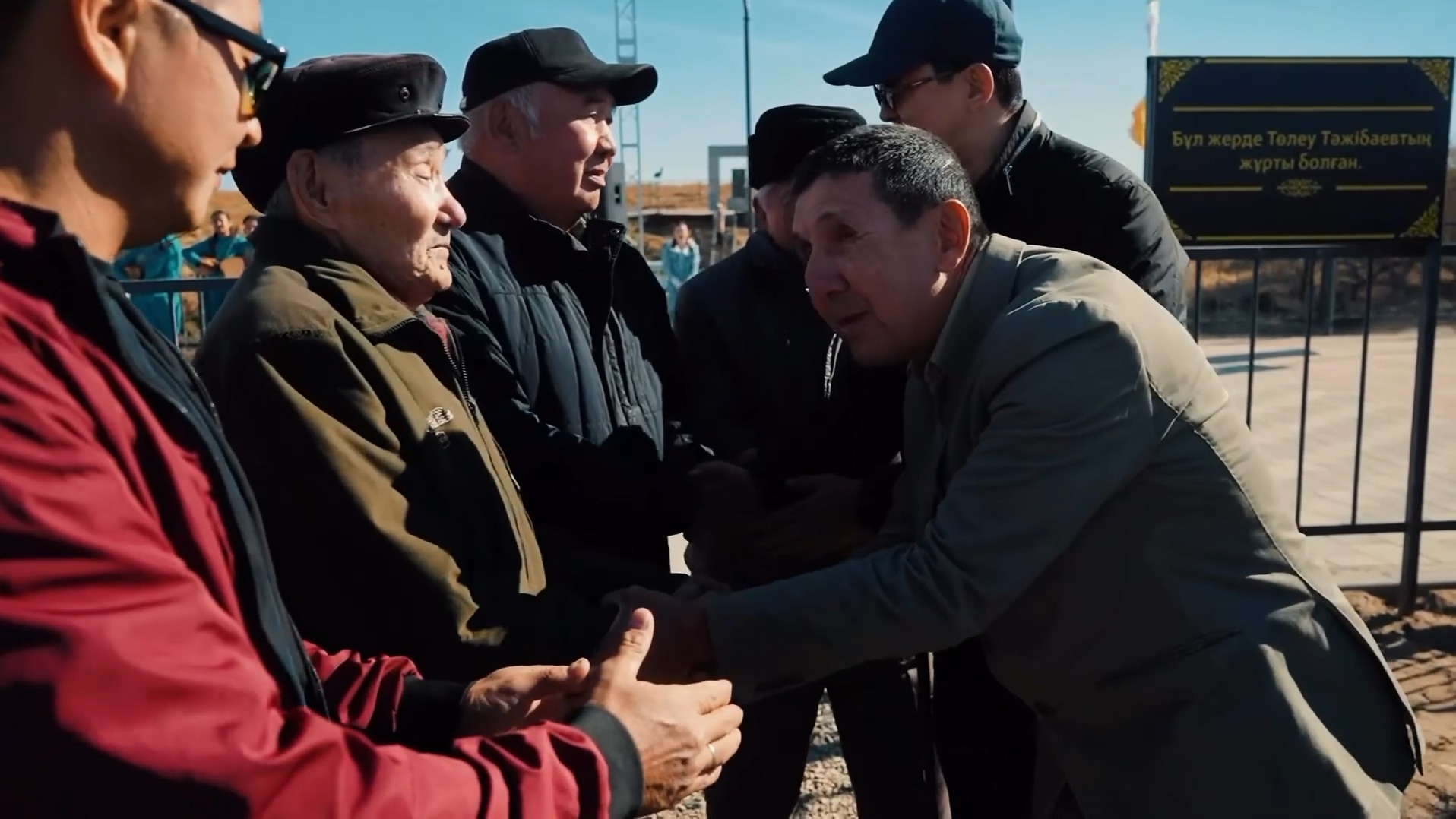 Костюм киген ер адамның қарттармен амандасып, сөйлесіп тұрған сәті.