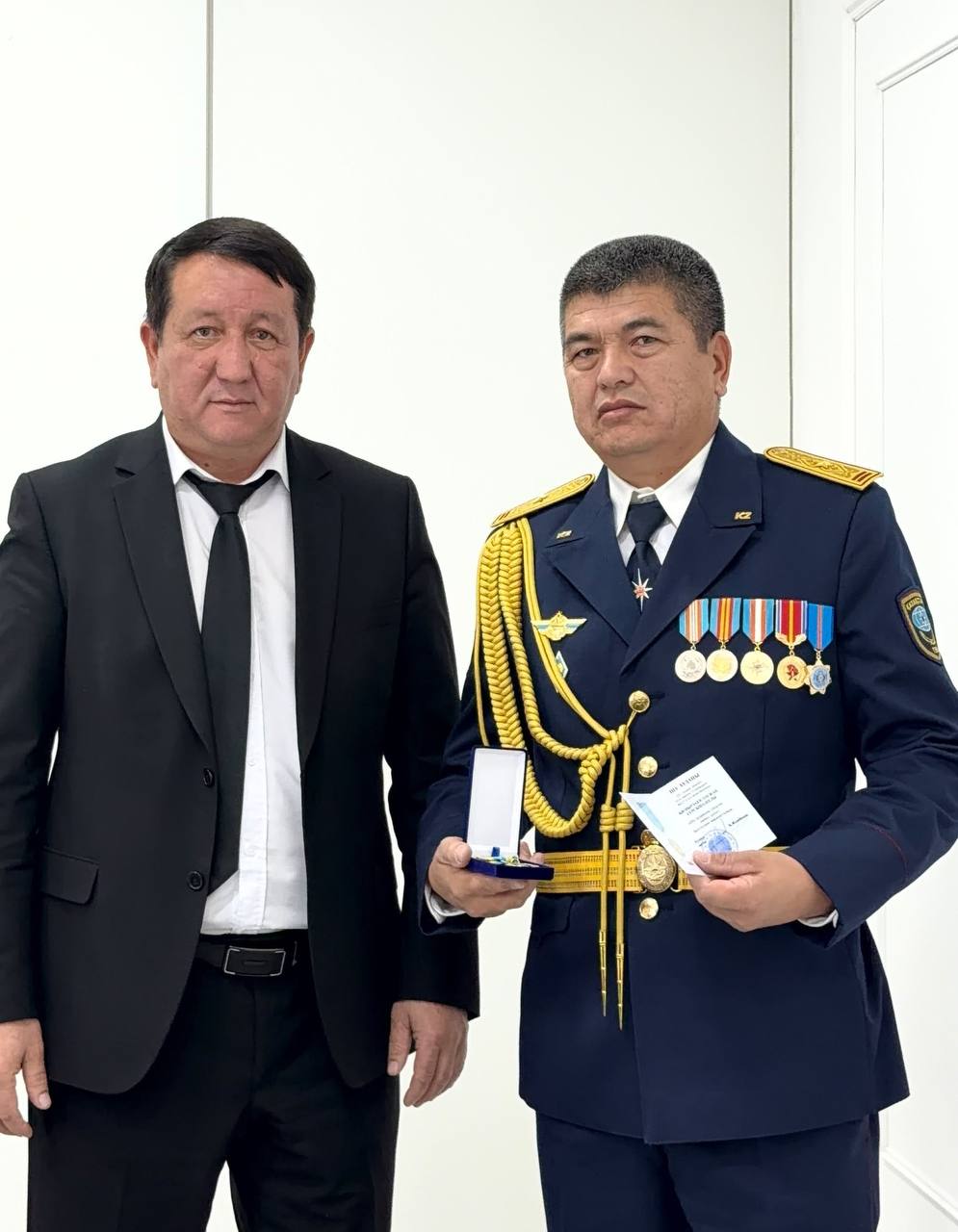 Костюм киген ер адам мен награда ұстаған әскери формадағы офицердің суреті.