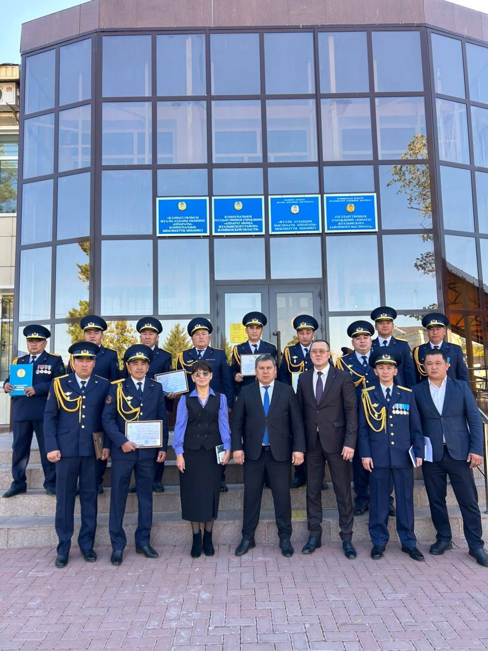 Форма киген әскери курсанттар мен ресми киінген адамдардың ғимарат алдындағы топтық суреті.