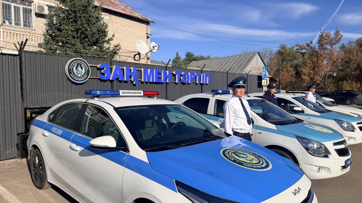 Полиция бөлімшесінің алдында тұрған полиция көліктері мен қызметкерлері.