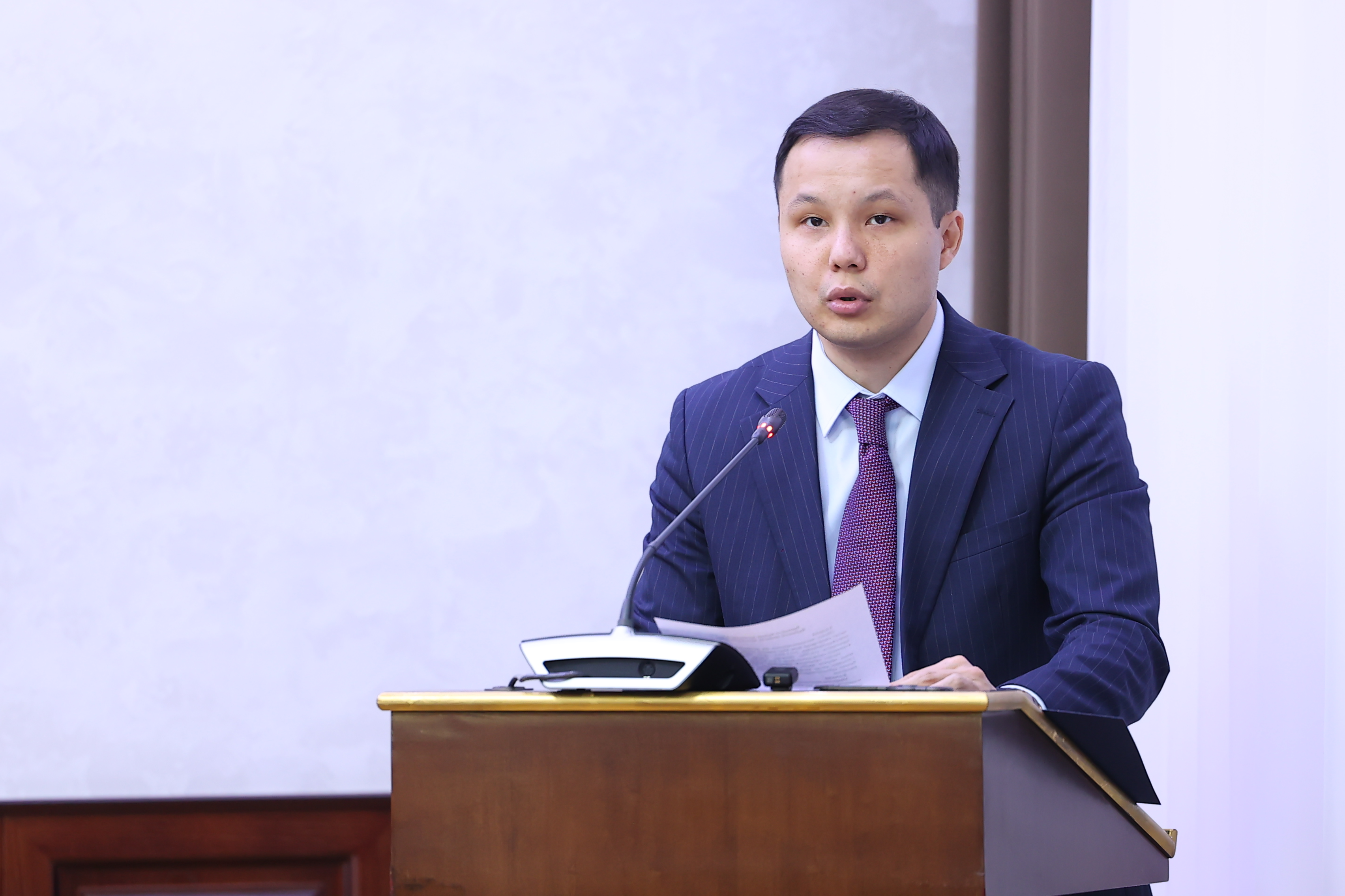 Кілемді костюм киген ер адам трибунада сөйлеп тұр.