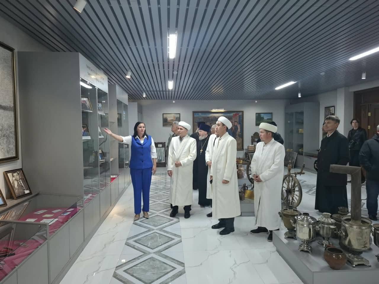 Мұражайда экспонаттарды таныстырып жатқан гид және діни қайраткерлер тобы.