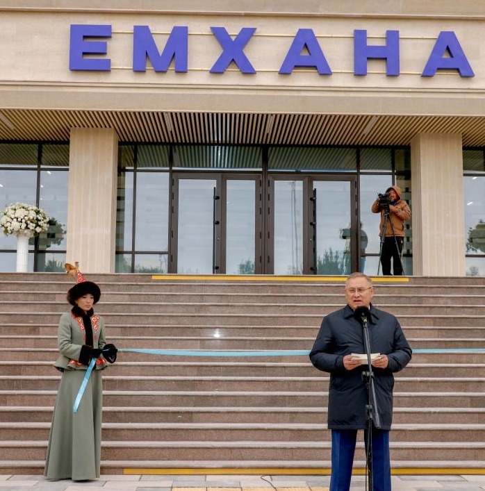 «ЕМХАНА» ғимаратының алдындағы салтанатты ашылу рәсімі: микрофонда сөйлеп тұрған ер адам және ұлттық киімдегі қыз.