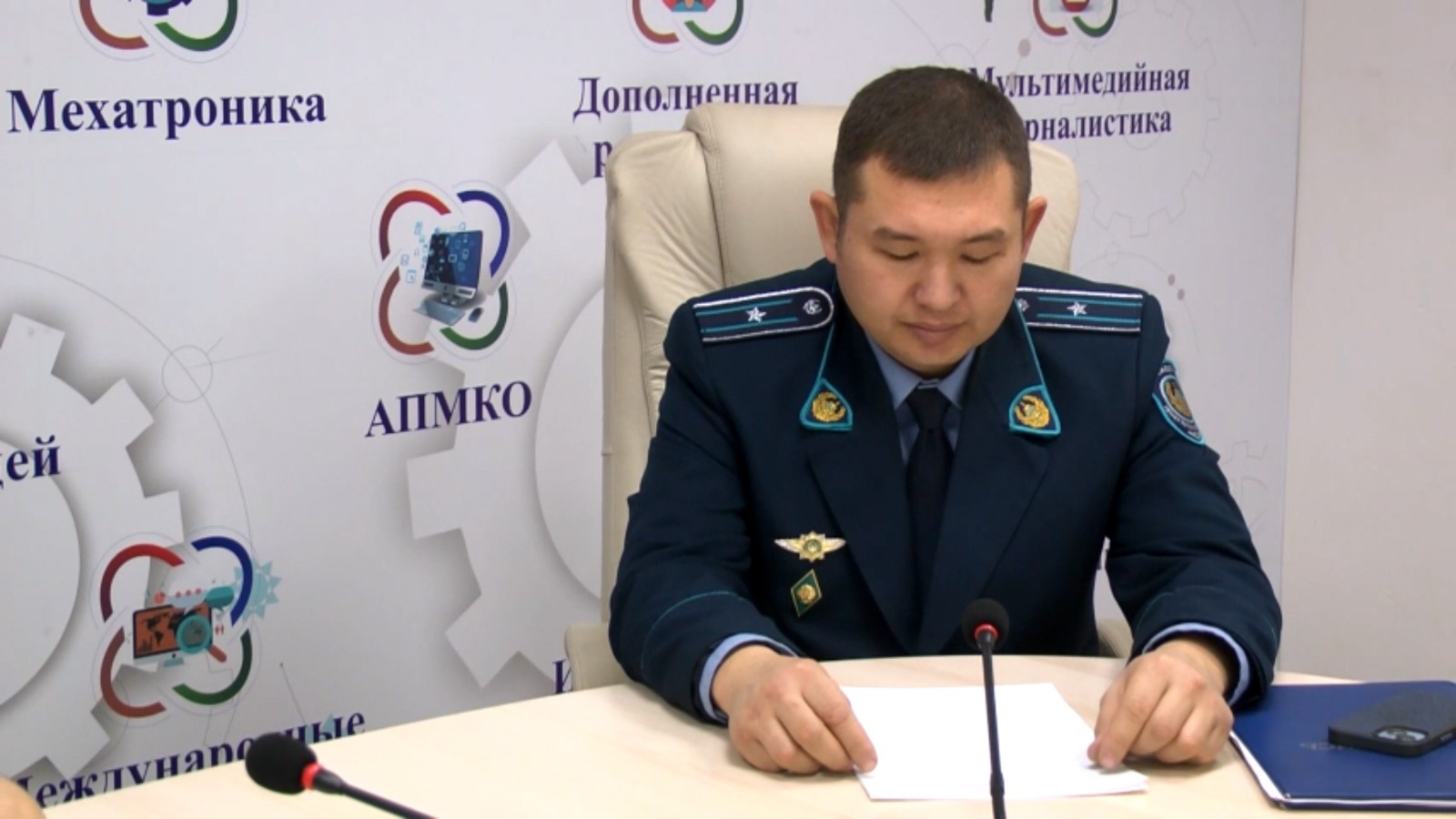 Көк форма киген әскери қызметші үстел басында қағазды оқып отыр.