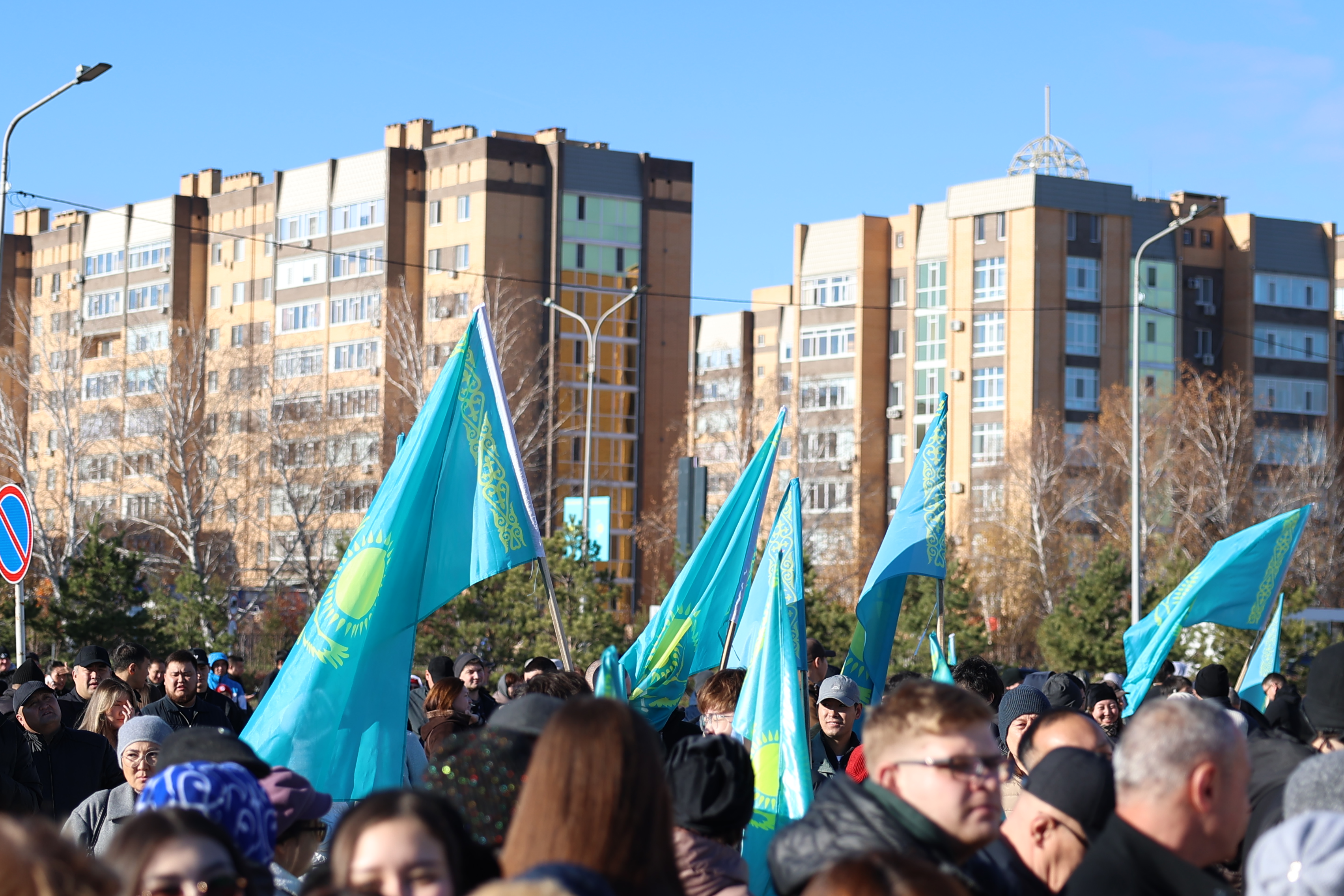 Қазақстан туларын ұстаған адамдардың көпшілігі және артқы фондағы тұрғын үйлер.