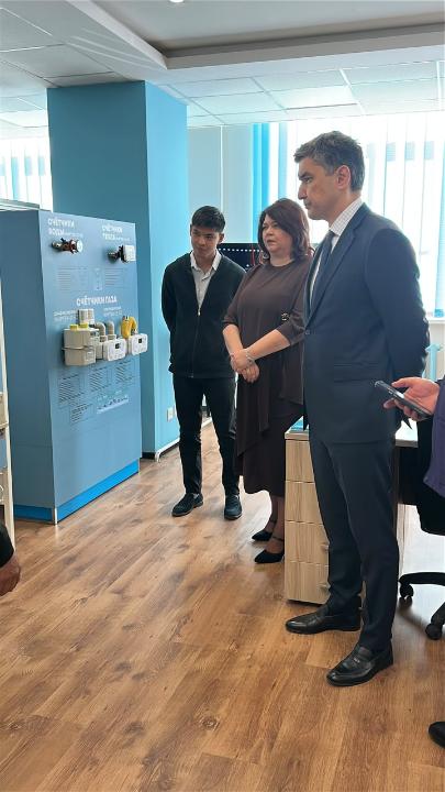 Көрсетілімдегі су және газ есептегіштерінің стенді алдында тұрған адамдар тобы.