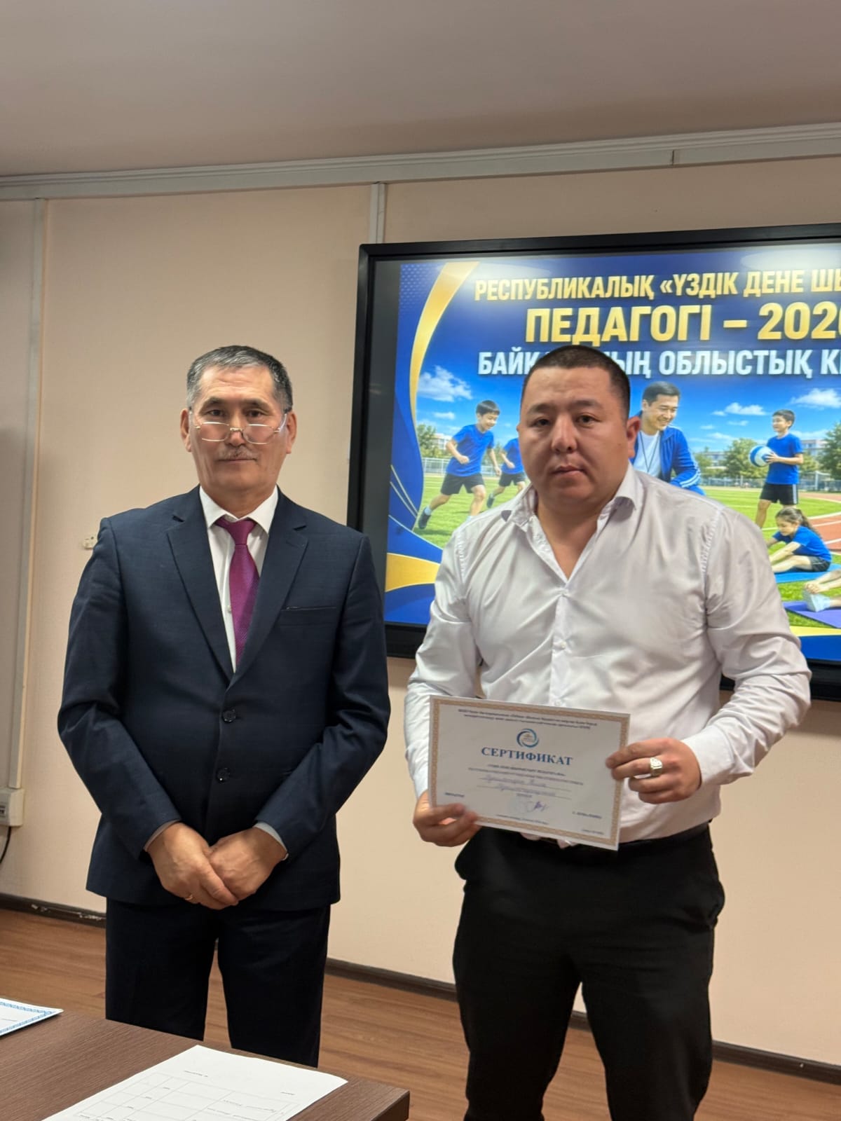 Сертификат алған ер адам мен костюм киген ер адамның фотосуреті.