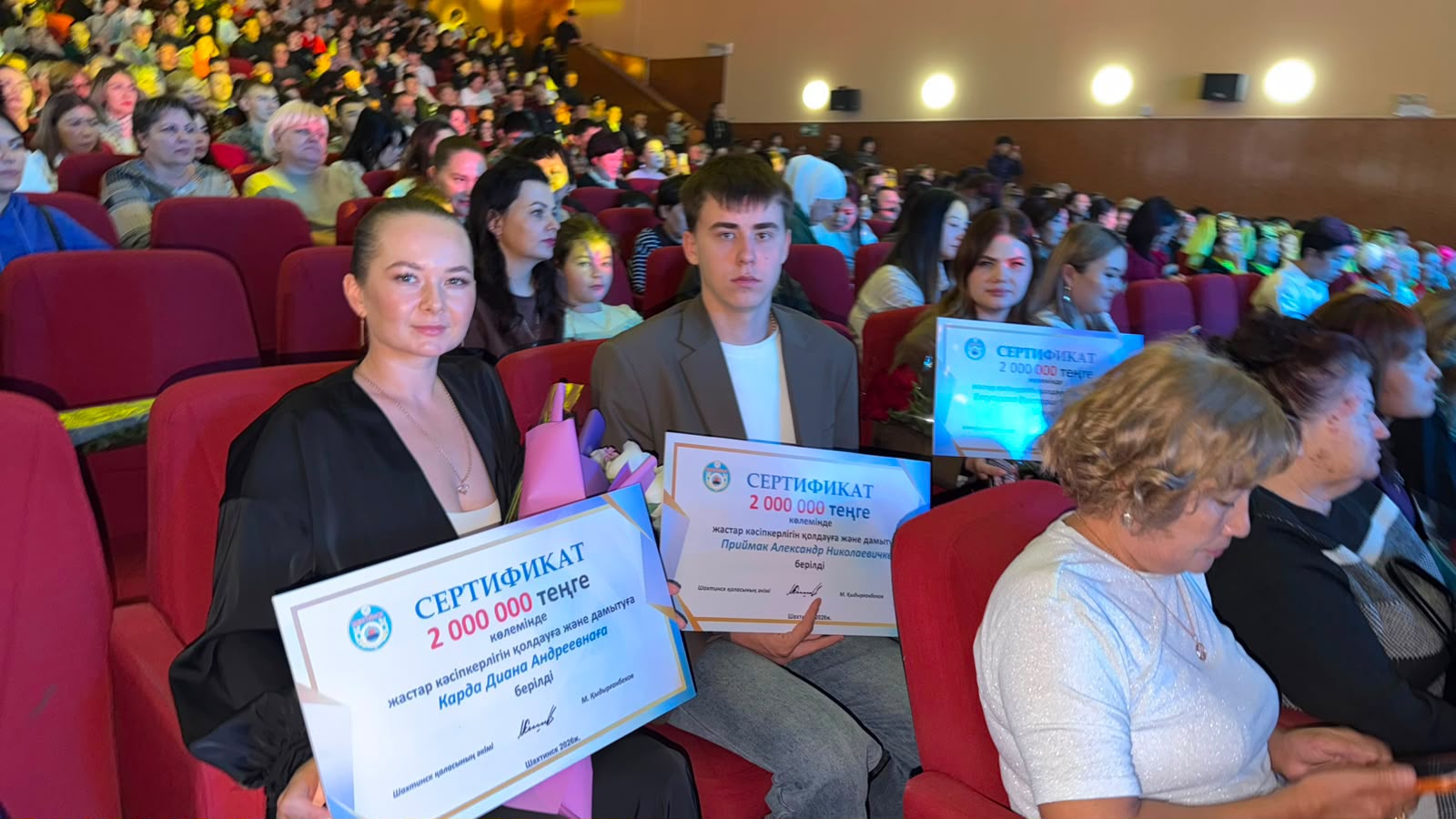 Салтқа жиналған адамдардың қолында 2 000 000 теңгелік грант сертификаттары бар суреті.