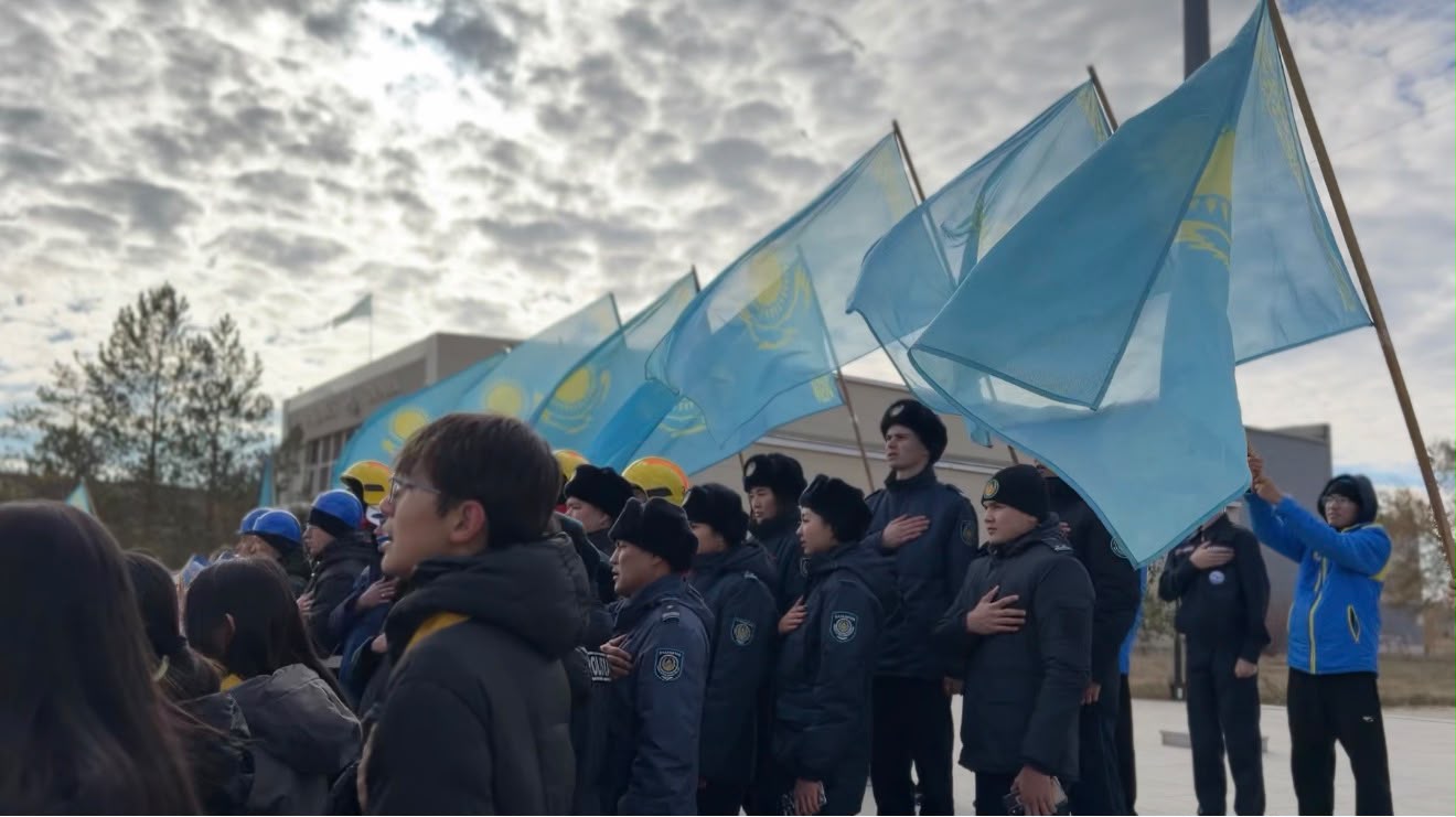 Қазақстан туларын ұстап тұрған және қолын жүрегіне қойған жастар тобы.