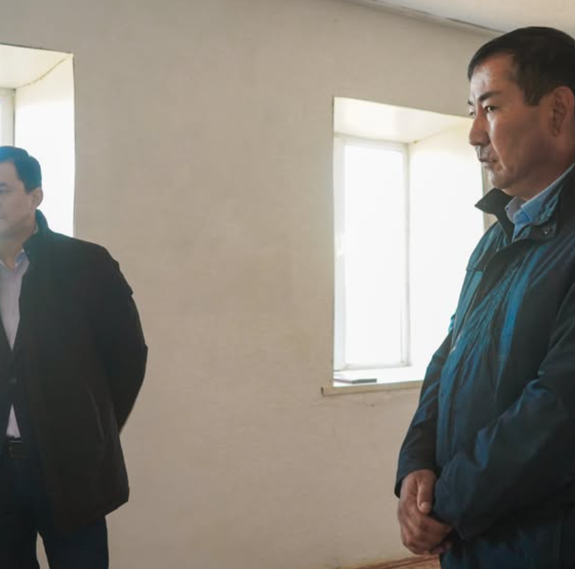 Бөлме ішінде тұрған екі ер адам.