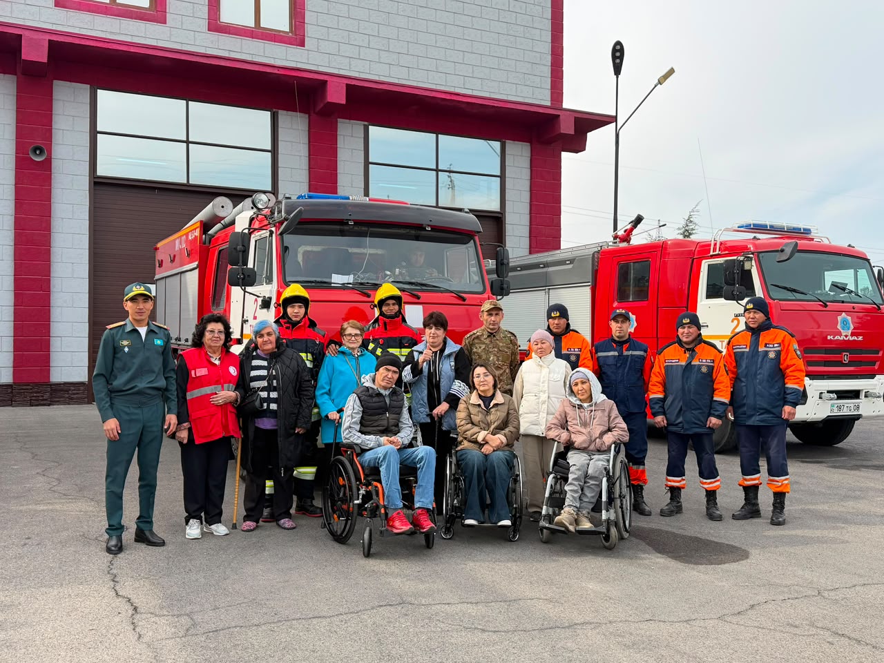 Өрт сөндіру техникасының жанында тұрған құтқарушылар мен мүмкіндігі шектеулі жандардың топтық суреті.
