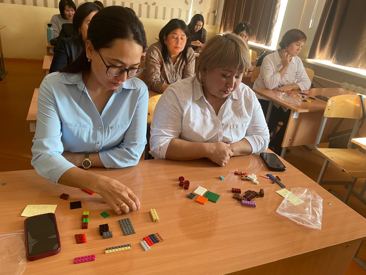 Үстел басында отырып, Lego бөлшектерімен жұмыс істеп жатқан әйелдер.