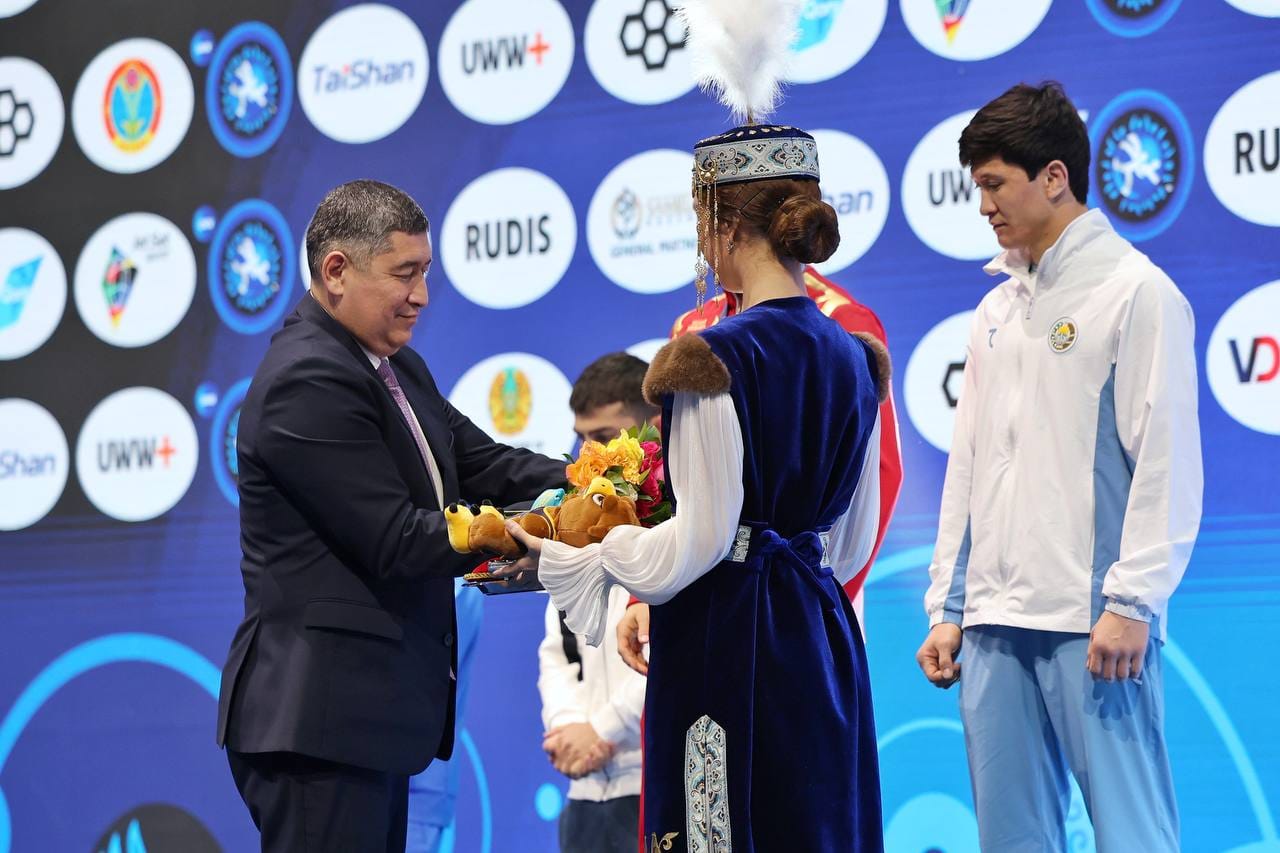 Костюм киген ер адам жеңімпазға гүл шоғын табыстап жатыр.