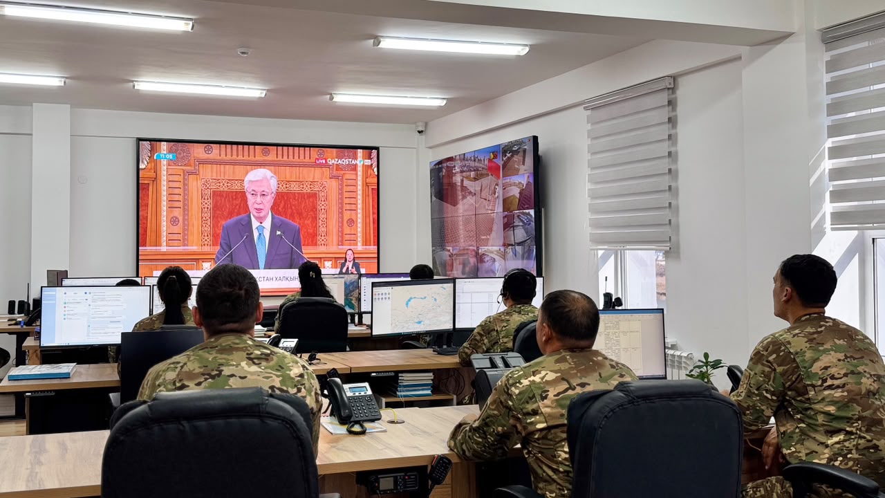 Военнослужащие в камуфляже смотрят выступление президента Казахстана на большом экране в оперативном центре.