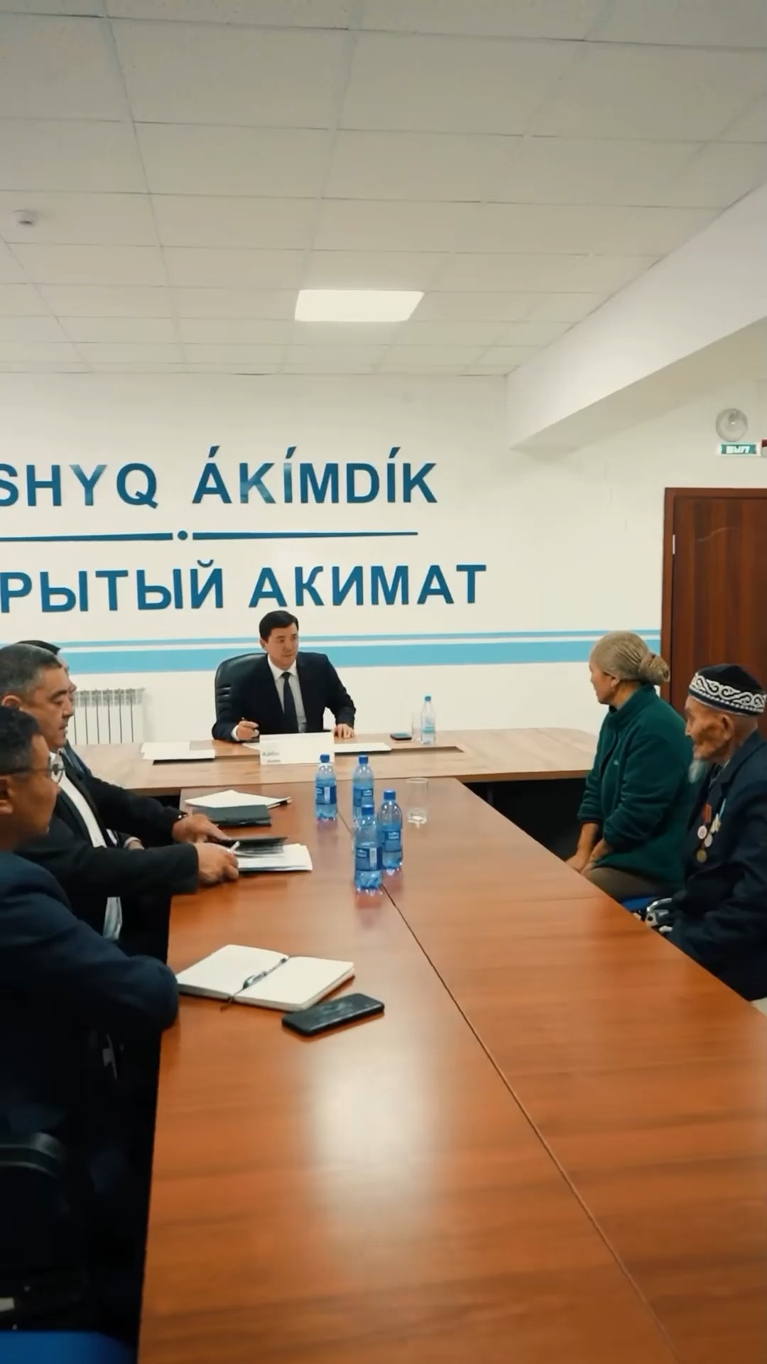 Әкімдіктегі жиналыс: ресми киінген шенеуніктер мен қариялардың келіссөздері.