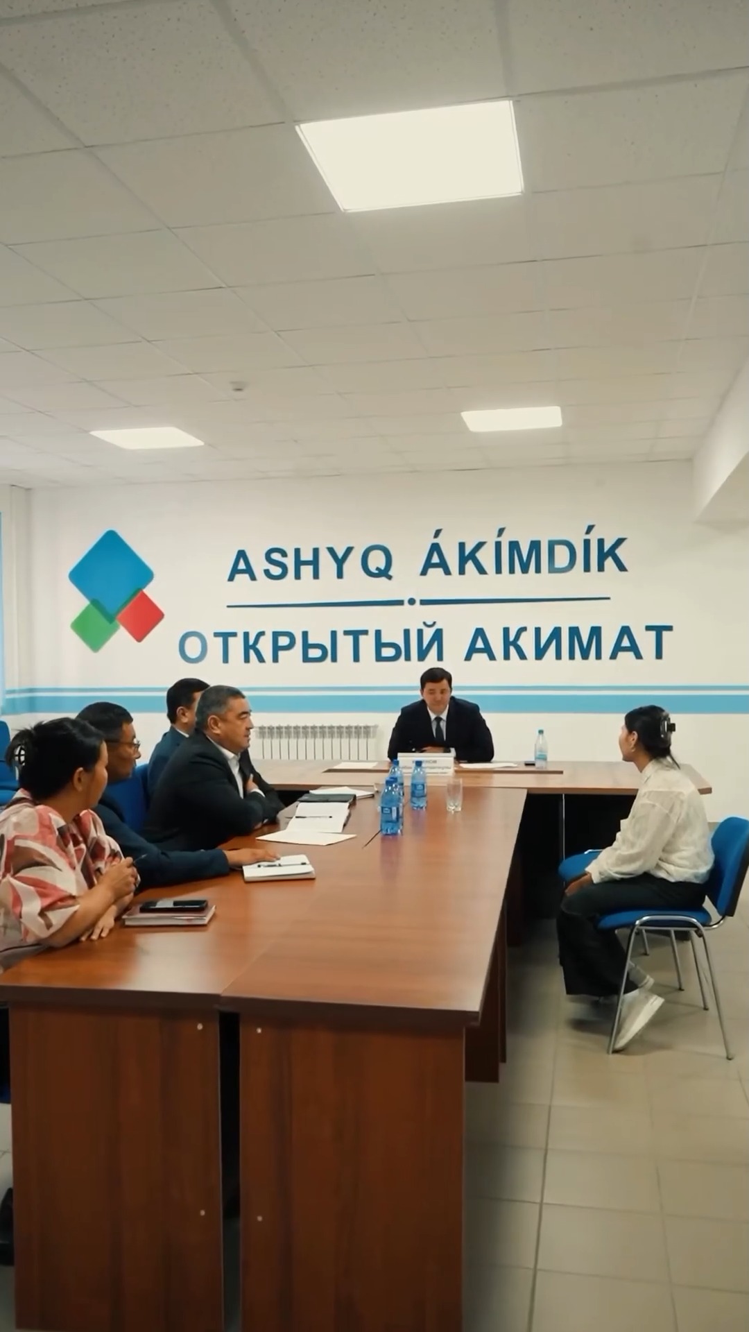 «Ashyq Ákimdik» кеңсесіндегі жиналыс: үстел басында отырған мемлекеттік қызметкерлер мен азаматтар.