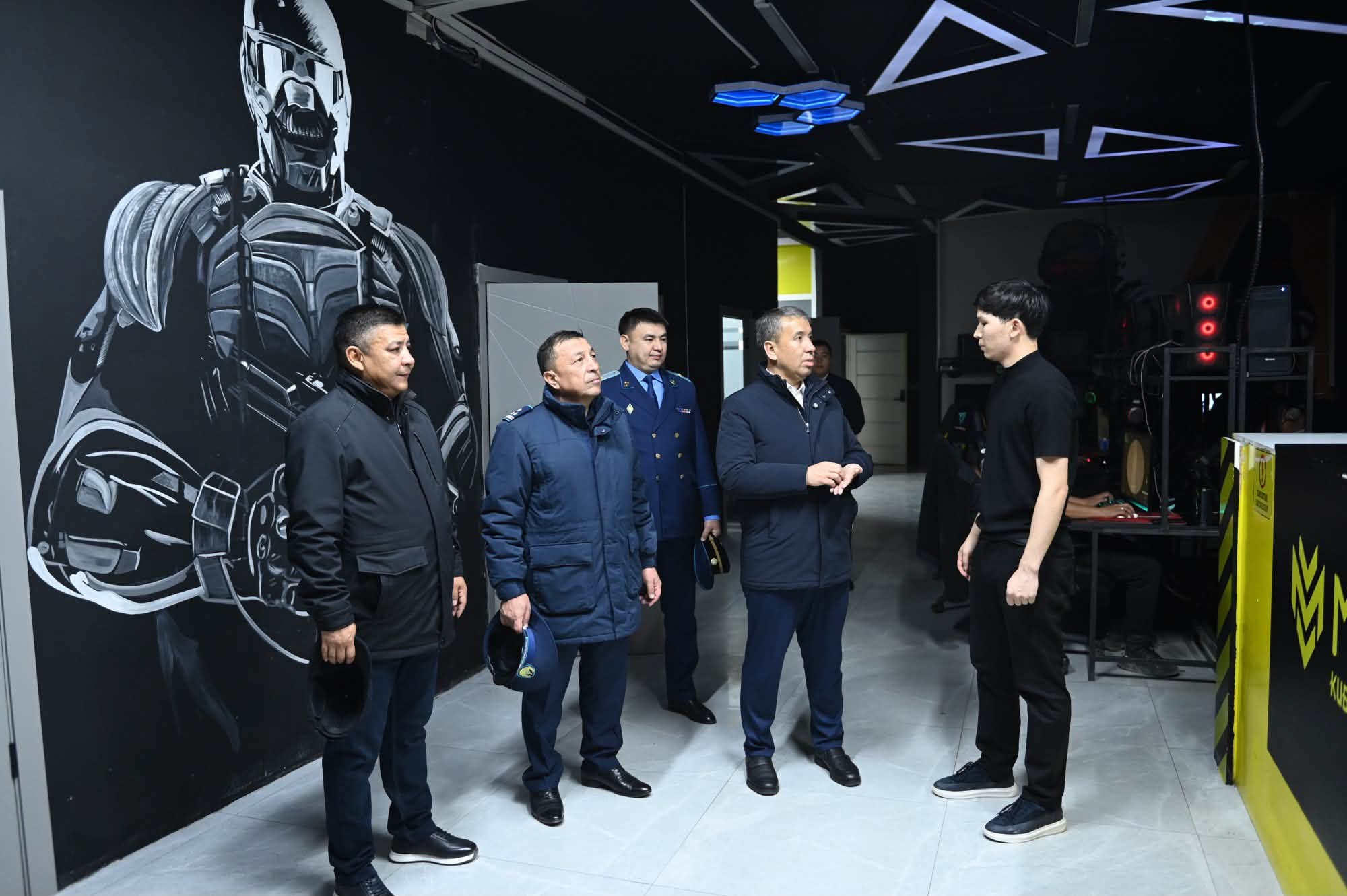 Технологиялық орталықдағы делегация мен маманның кездесуі. Фонда робот бейнесі бейнеленген қабырға тұр.