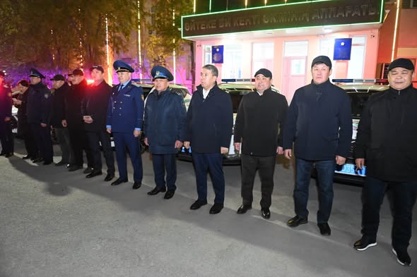Форма киген және қара киімді ерлер тобы ғимарат алдында тізіліп тұр.