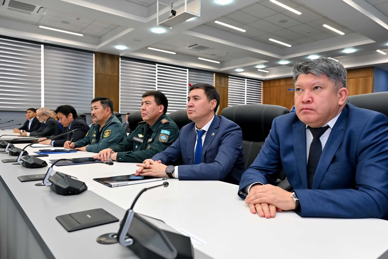 Жиналыс үстіндегі костюм киген ресми тұлғалар мен әскери формадағы офицерлер.