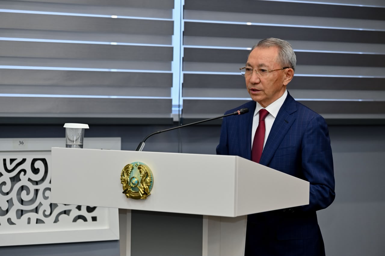 Көк костюм киген ер адам трибунада сөйлеп тұр.