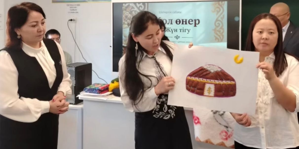 Үш әйел қол өнер сабағында ұлттық киімнің суретін көрсетіп тұр.