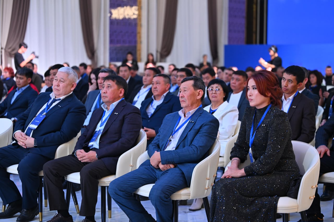 Конференцияда отырған ресми киінген адамдар тобы.