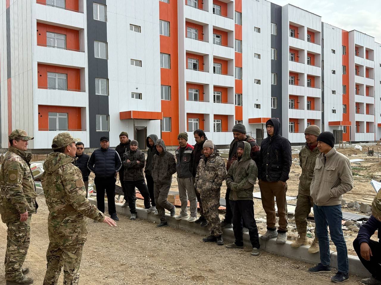 Жаңа тұрғын үйлердің алдында әскери формадағы адамдар мен жастардың жиналысы.