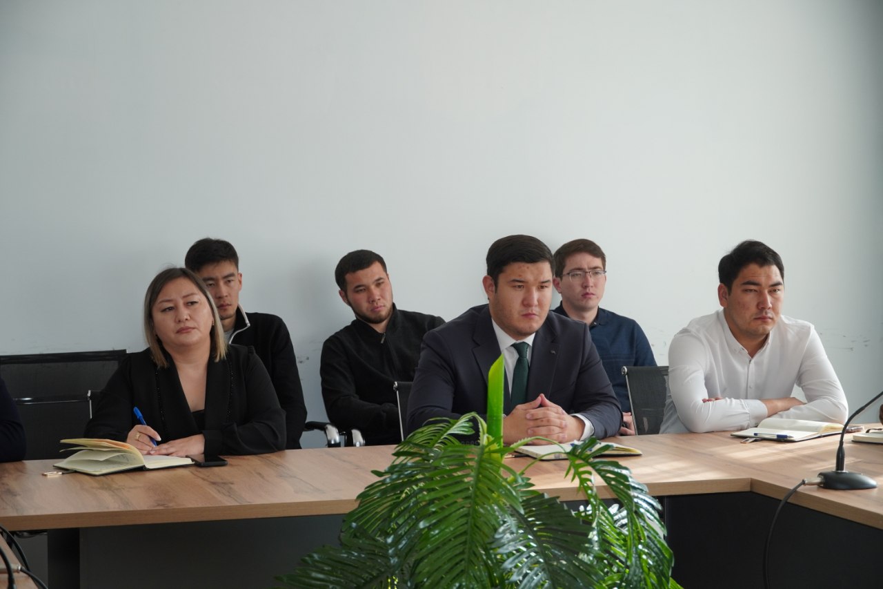 Кеңседе үстел басында отырған алты адамның тобы.