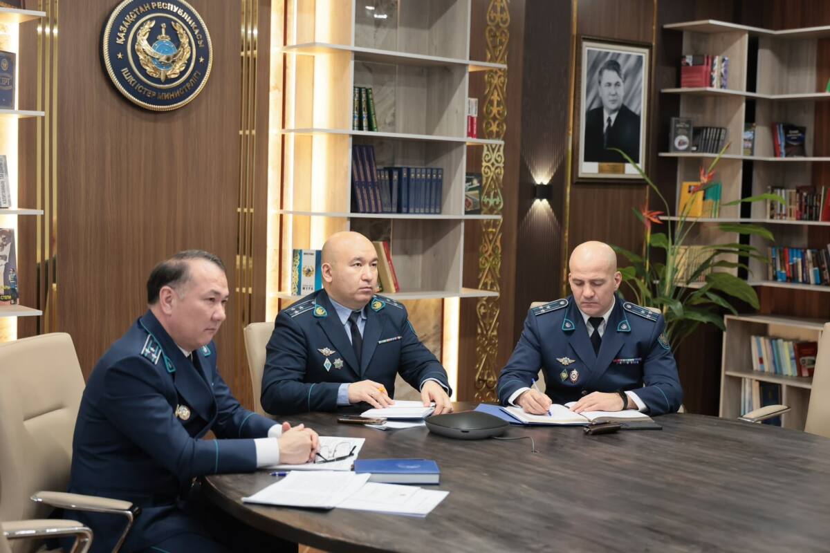 Көк форма киген үш әскери қызметкер жиналыс үстелінде құжаттармен жұмыс істеп отыр.